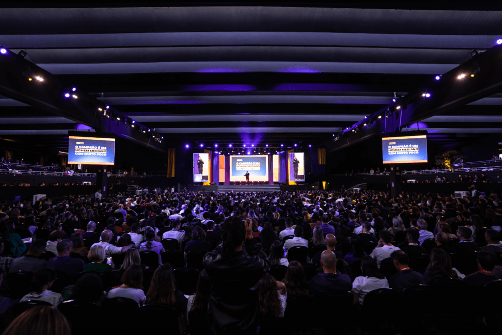 Auditório lotado do Sev7n Summit: milhares de participantes sentados de frente para o palco, contexto em que um formulário passivo de qualificação se perderia.